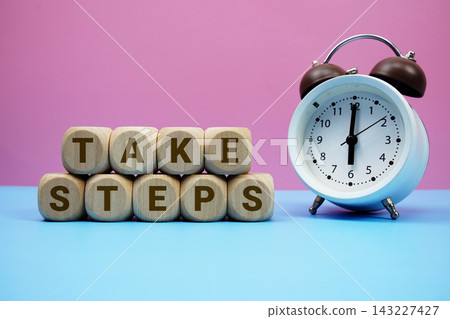 Take Steps alphabet letters wooden cube with alarm clock on pink and blue background Take Steps alphabet letters wooden cube with alarm clock on pink and blue background 143227427
