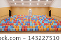 3D render of an empty auditorium featuring rows of colorful seats, wooden steps, orange walls, and a projector booth. 143227510