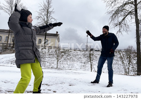 Joyful young boy throwing homemade snowball at his smiling dad inside public city park during winter walk. Joyful young boy throwing homemade snowball at his smiling dad inside public city park during winter walk. 143227978