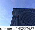 Dark corrugated metal building corner with security camera against clear blue sky 143227987