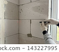 A construction worker measures a concrete block wall with a laser distance meter. Interior renovation, building measurement, and professional craftsmanship. 143227995