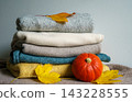 An orange pumpkin and autumn leaves rest beside folded knitwear. Concept of autumn, warmth, harvest, comfort, clothing, seasonality and home comfort 143228555