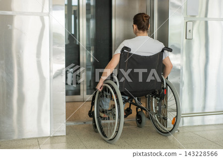 A Caucasian woman in a wheelchair uses an elevator. A Caucasian woman in a wheelchair uses an elevator. 143228566