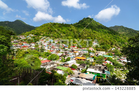 Scenic view of colorful homes tucked into lush green tropical mountains in the village of Soufriere on the Caribbean island of Dominica. Scenic view of colorful homes tucked into lush green tropical mountains in the village of Soufriere on the Caribbean island of Dominica. 143228885