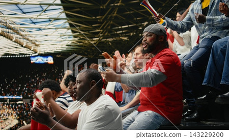 Shocked black fan celebrating betting lucky win with adrenaline, jumping with his friends after final whistle inside the stadium. Excited fan reacts to winning ticket mobile bet, jackpot thrill. 143229200