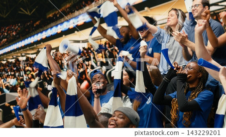 Blue football supporters cheering in packed stadium fan section during intense live soccer match, scarves, horns and crowd reaction. Sports fans wearing face paint for game excitement. Blue football supporters cheering in packed stadium fan section during intense live soccer match, scarves, horns and crowd reaction. Sports fans wearing face paint for game excitement. 143229201