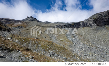 Panoramic mountain views during the Grossglockner hike, alpine mountain landscape with rugged rocky terrain, snowfields, distant peaks, glacier remnants, and a stone cairn Panoramic mountain views during the Grossglockner hike, alpine mountain landscape with rugged rocky terrain, snowfields, distant peaks, glacier remnants, and a stone cairn 143230364