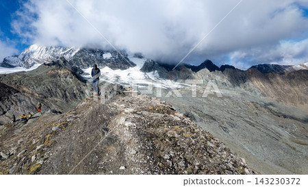 View of Grossglockner from near Studl Hut in the Austrian Alps, dramatic glaciated mountain landscape with hikers on a rocky ridge beneath clouds and blue sky View of Grossglockner from near Studl Hut in the Austrian Alps, dramatic glaciated mountain landscape with hikers on a rocky ridge beneath clouds and blue sky 143230372