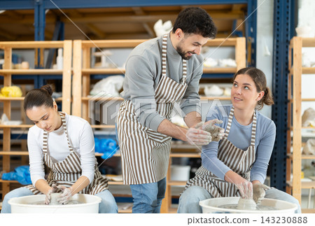 Girl craftsperson busy molding clay products using pottery wheel in lesson with male teacher Girl craftsperson busy molding clay products using pottery wheel in lesson with male teacher 143230888