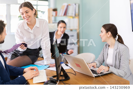 Young woman flirting with male colleague while sitting on office desk Young woman flirting with male colleague while sitting on office desk 143230969