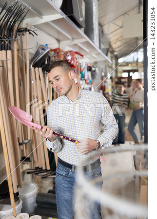 Young man choosing shovel in store 143231054