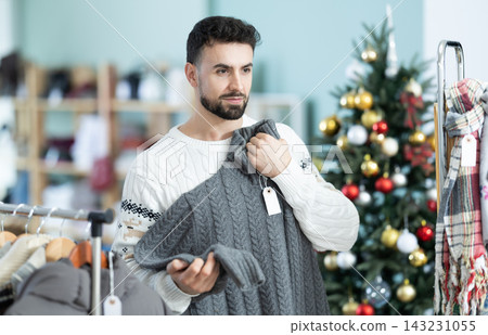 Young man chooses sweater in clothing store Young man chooses sweater in clothing store 143231055