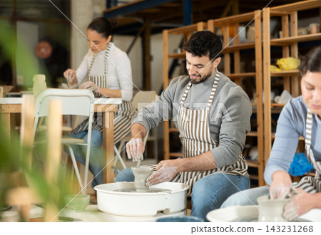 Man in ceramics workshop with pottery wheel and various clay vessels 143231268