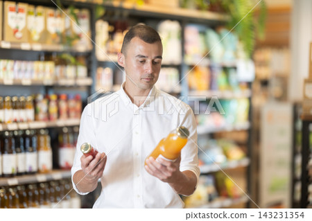 Interested man pondering choices of organic juices in natural food store 143231354
