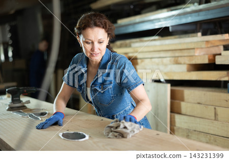 Female sawmill worker cleaning up excess resin or glue on wooden board Female sawmill worker cleaning up excess resin or glue on wooden board 143231399