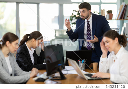 Young man standing and scolding sad seated colleagues in office Young man standing and scolding sad seated colleagues in office 143231420