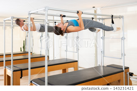 Girl and man do pilates suspended on special sports equipment Girl and man do pilates suspended on special sports equipment 143231421