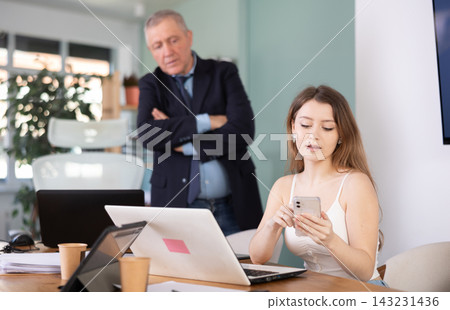 Elderly man scolding young female colleague for sitting with mobile phone Elderly man scolding young female colleague for sitting with mobile phone 143231436