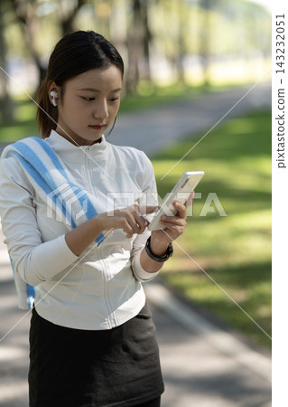 Young Asian Woman Using Smartphone with Wireless Earbuds During Outdoor Workout in Park Young Asian Woman Using Smartphone with Wireless Earbuds During Outdoor Workout in Park 143232051