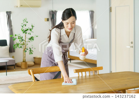 一位年輕的日本女子用噴霧瓶擦拭桌子。 一位年輕的日本女子用噴霧瓶擦拭桌子。 143237162