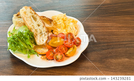 Healthy breakfast with scrambled eggs, toasted, sliced cherry tomato, and fresh greens on wooden surface. 143239281