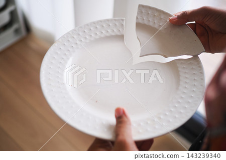 Person holds a broken piece of a plate in a room with wooden flooring 143239340