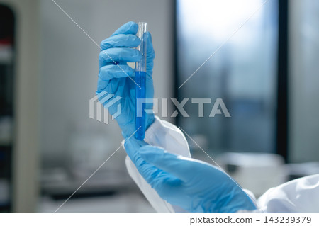 Scientist gloved hand holding glass test tube with blue liquid in laboratory setting 143239379