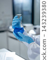 Scientist wearing blue gloves holding flask with blue liquid in modern laboratory setting 143239380