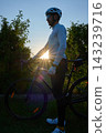 Cyclist in a helmet stands beside his bicycle outdoors at sunset 143239716