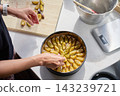 Woman arranging sliced plums on dough while making pie in kitchen. 143239721