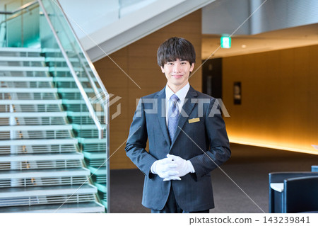 男性工作人員微笑著迎接客人,並在大廳和樓梯頂端提供協助。 男性工作人員微笑著迎接客人,並在大廳和樓梯頂端提供協助。 143239841