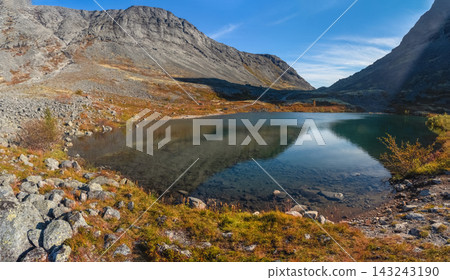 Pristine mountain lake with clear water and rocky shores in Khibiny mountains under blue sky, Kola Peninsula, Arctic Russia. 143243190