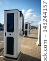 Row of electric vehicle fast charging stations on stone paved sidewalk under blue cloudy sky 143244157
