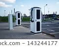 Brand new electric car charging stations wrapped in protective plastic film on empty urban parking lot under blue sky 143244177