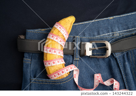 Banana with measuring tape on jean trousers, penis health. Banana with measuring tape on jean trousers, penis health. 143244322