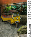 Classic yellow Thai Tuk Tuk three wheeler vehicle parked in a garden. 143244419