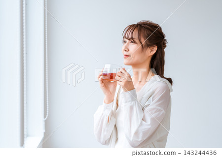一位女士放鬆地啜飲著熱茶,凝視著窗外。 一位女士放鬆地啜飲著熱茶,凝視著窗外。 143244436
