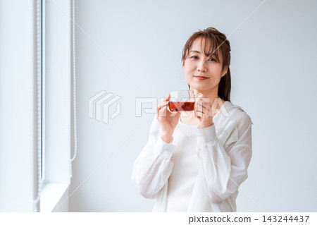 一位女士放鬆地啜飲著熱茶,凝視著窗外。 一位女士放鬆地啜飲著熱茶,凝視著窗外。 143244437
