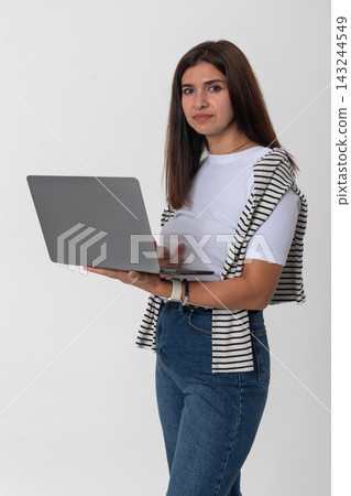 Young woman standing on a white background, holding an open laptop in her hands, looking at the camera while embodying concepts of technology, connectivity, and remote working Young woman standing on a white background, holding an open laptop in her hands, looking at the camera while embodying concepts of technology, connectivity, and remote working 143244549