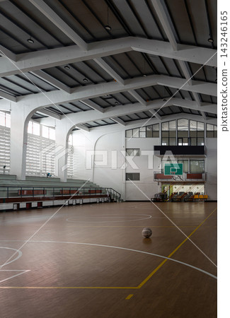 a single basketball sits amidst subtle gradients of light and shadow, framed by soaring structural beams, tiered concrete bleachers, and a vintage green backboard. a single basketball sits amidst subtle gradients of light and shadow, framed by soaring structural beams, tiered concrete bleachers, and a vintage green backboard. 143246165