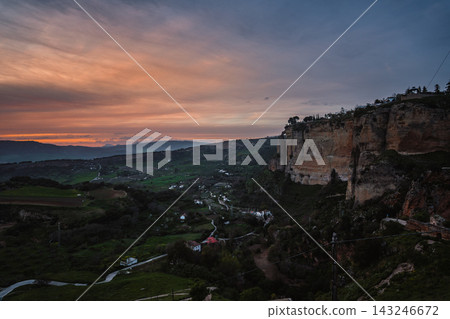 Ronda limestone cliffs and green valley under an orange sunset sky Ronda limestone cliffs and green valley under an orange sunset sky 143246672