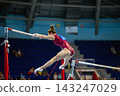 Female gymnast performing routine on uneven bars 143247029