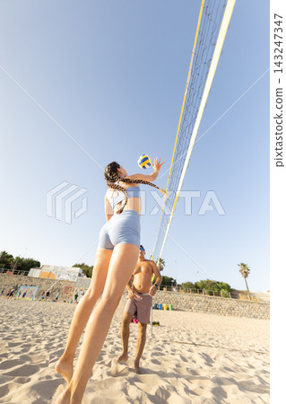Volleyball game on the beach under clear sky with players on sand and net 143247347