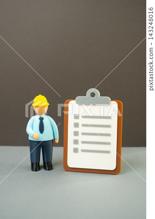Official in a yellow hard hat with a paper clipboard. Inspections and tests. Audits and occupational safety standards. Construction compliance, workplace regulations and quality control. Official in a yellow hard hat with a paper clipboard. Inspections and tests. Audits and occupational safety standards. Construction compliance, workplace regulations and quality control. 143248016