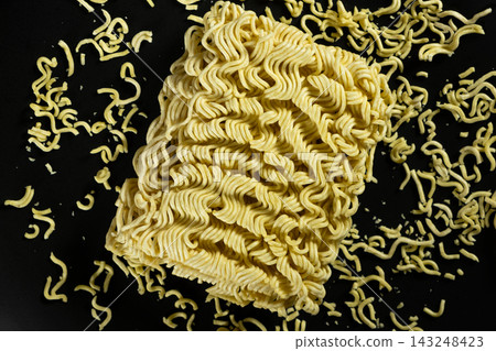 Raw instant ramen noodle block with scattered small noodle bits on black background Raw instant ramen noodle block with scattered small noodle bits on black background 143248423