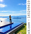 A woman stands at Biwako Terrace, overlooking the clear blue sky and Lake Biwa. 143249419