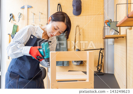 一位日本女子在DIY工作室用電鑽組裝一張木椅。 一位日本女子在DIY工作室用電鑽組裝一張木椅。 143249623