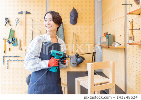一位微笑的日本女子正在DIY工作室用電鑽檢查一張已經做好的木椅。 一位微笑的日本女子正在DIY工作室用電鑽檢查一張已經做好的木椅。 143249624
