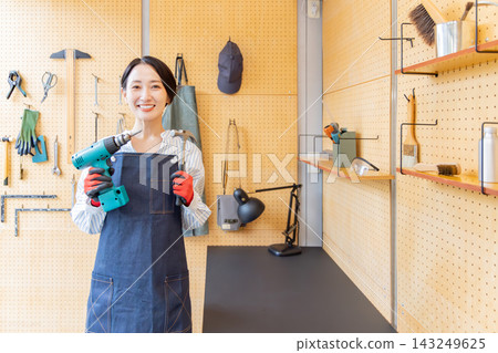一位微笑的日本女性在DIY工作室裡拿著電鑽和鐵鎚。 一位微笑的日本女性在DIY工作室裡拿著電鑽和鐵鎚。 143249625