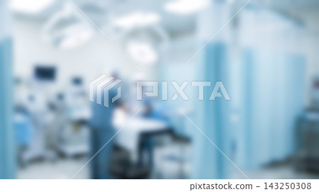 Defocused surgery room interior showing professional surgeons performing medical operation around operating table illuminated by large overhead lamps inside busy clinic department 143250308